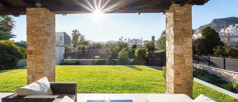 A covered outdoor seating area with stone pillars, a view of a grassy yard, and a mountain in the background.
