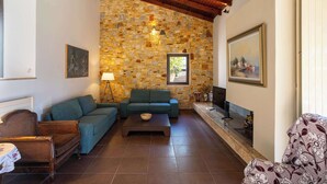 A living room with a stone wall, a sofa, a coffee table, and a fireplace. - Villa Amorata - Schinias Private Garden Retreat (Schinias)