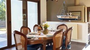 A dining area with a table set for six, surrounded by wicker chairs, a vase with flowers, and a hanging boat decoration. - Villa Amorata - Schinias Private Garden Retreat (Schinias)