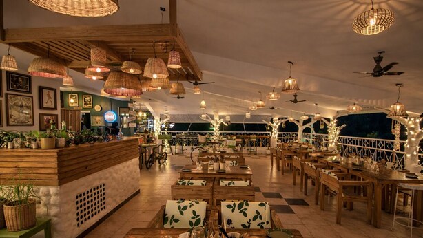 Ein geräumiges Restaurant mit Holztischen und -stühlen, hängenden Korbstühlen und einer Theke mit Pflanzen und Fahrrädern.