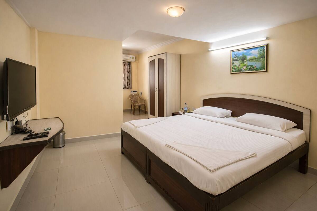 A hotel room with a bed, a desk with a TV, a chair, and a painting on the wall.