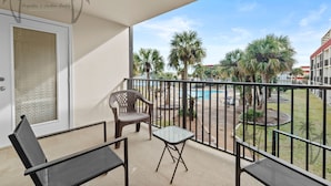 A balcony with a pool view, a chair, a small table, and a door with frosted glass. - Ocean Club Villa D-206 | Your Coastal Paradise Awaits! (Biloxi)