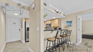 A kitchen with wooden cabinets, a microwave, and a sink. There are three bar stools with cushioned seats. - Ocean Club Villa D-206 | Your Coastal Paradise Awaits! (Biloxi)
