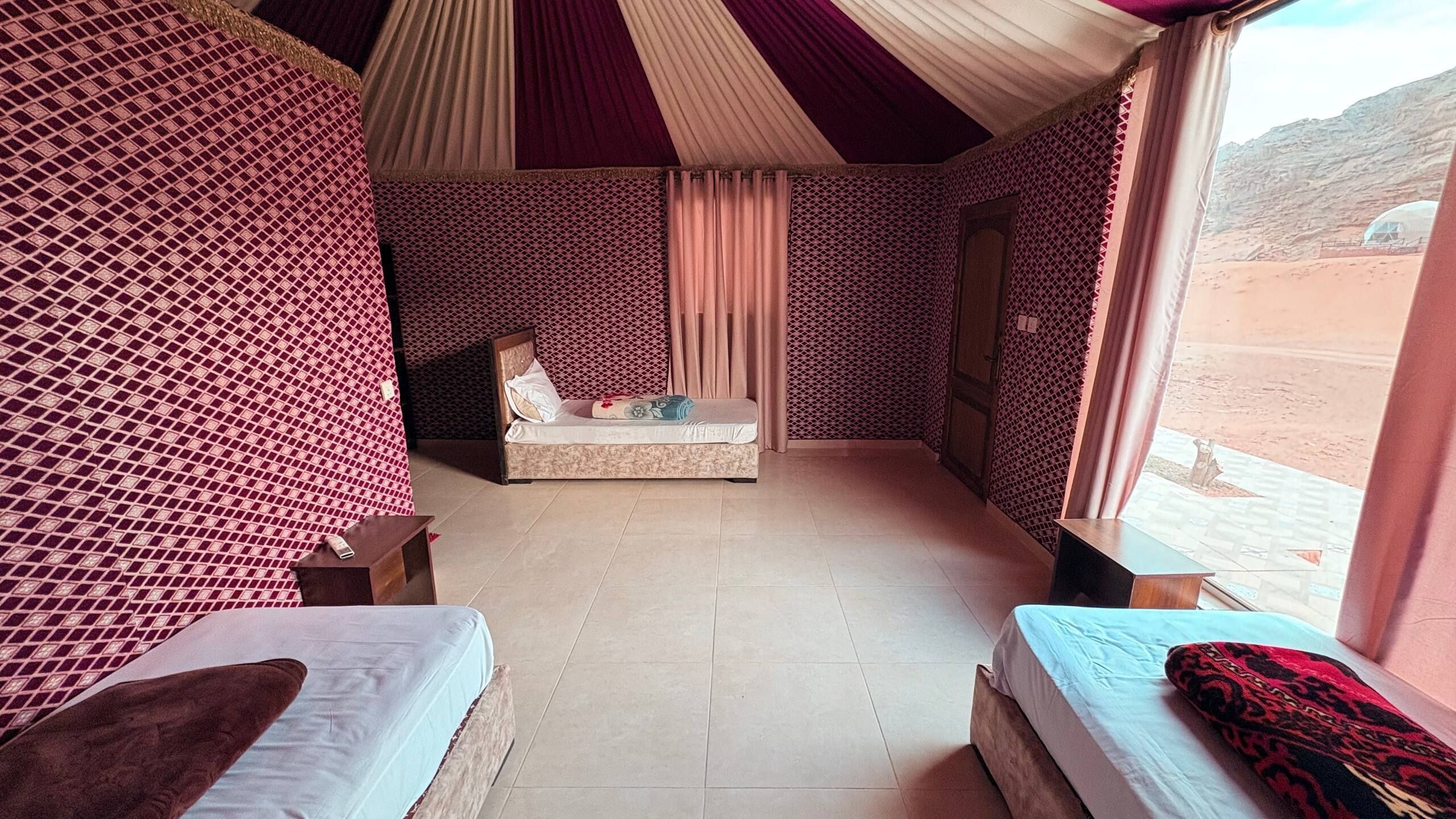 A room with two beds, a sofa, a patterned wall, and a view of a desert landscape.