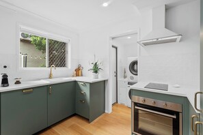 A compact kitchen with a built-in oven, a washing machine, and a window with a view of greenery. - Palm-Feel Townhouse in the Heart of Burleigh (Burleigh Heads)