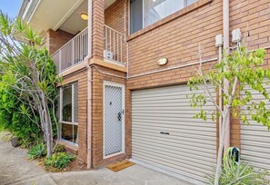 A two-story brick building with a garage door, a small balcony, and a welcome mat. - Palm-Feel Townhouse in the Heart of Burleigh (Burleigh Heads)