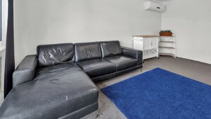 A black leather sofa, a blue rug, a white cabinet, and an air conditioning unit in a room with white walls.