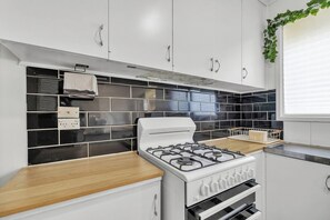 Una cocina con estufa a gas, muebles blancos, azulejos blanco y negro, y encimera de madera.