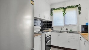A kitchen with white cabinets, a stove, an oven, a microwave, and a window with blinds.