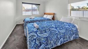 A bedroom with two beds, a wooden headboard, a window with blinds, and a view of a fenced area outside.