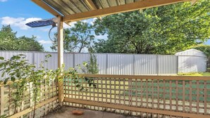 A covered patio area with a wooden fence, a solar panel, and a small brick object on the ground.