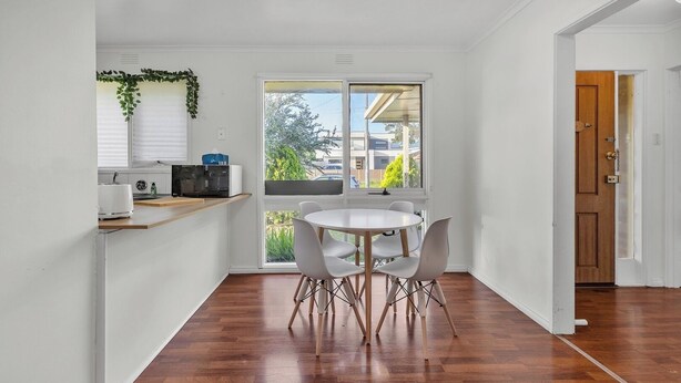 A compact kitchen with a dining area, a wooden floor, and a view through a large window.