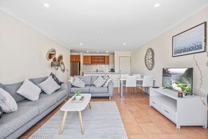 A modern living room with a grey sofa, a coffee table, and a TV. - Sunny, Stylish Island Stay Minutes from Surfers (Surfers Paradise)