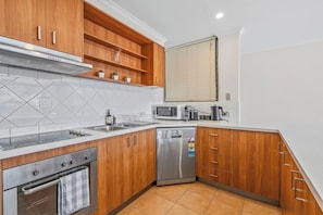 A modern kitchen with wooden cabinets, a stainless steel dishwasher, a microwave, and a stove. - Sunny, Stylish Island Stay Minutes from Surfers (Surfers Paradise)