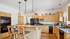 A kitchen with wooden cabinets, a central island with stools, a refrigerator, microwave, oven, and a sink.