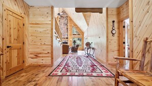 A wooden interior with a central rug, wooden walls, a staircase, and a clock on the wall.