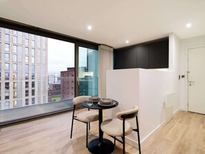 Ein modernes Hotelzimmer mit einem großen Fenster, einem runden Tisch mit zwei Stühlen und einer weißen Tür.