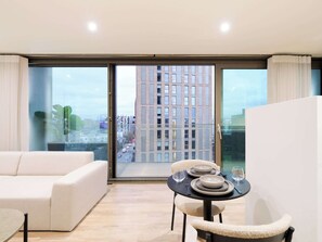Ein modernes Wohnzimmer mit einer Couch, einem Esstisch für zwei Personen und einer großen Schiebeglastür mit Blick auf die Stadt.