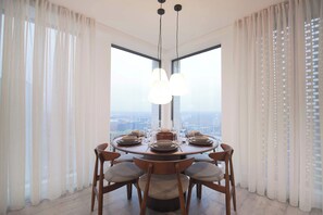 A dining area with a round table set for six, large windows, and a city view. - Midori | The Heim (Manchester)