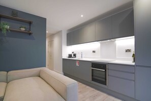 A modern kitchen with grey cabinets, a built-in oven, and a countertop with a sink. - Midori | The Heim (Manchester)