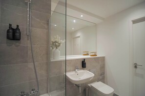 A modern bathroom with a glass shower enclosure, a white sink, and a toilet. - Midori | The Heim (Manchester)