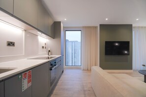 A modern kitchen with a large window, a flat-screen TV, and a sofa in a living area. - Midori | The Heim (Manchester)