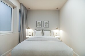 Una camera da letto con un letto, due comodini, una finestra con tende e due lampade a parete.