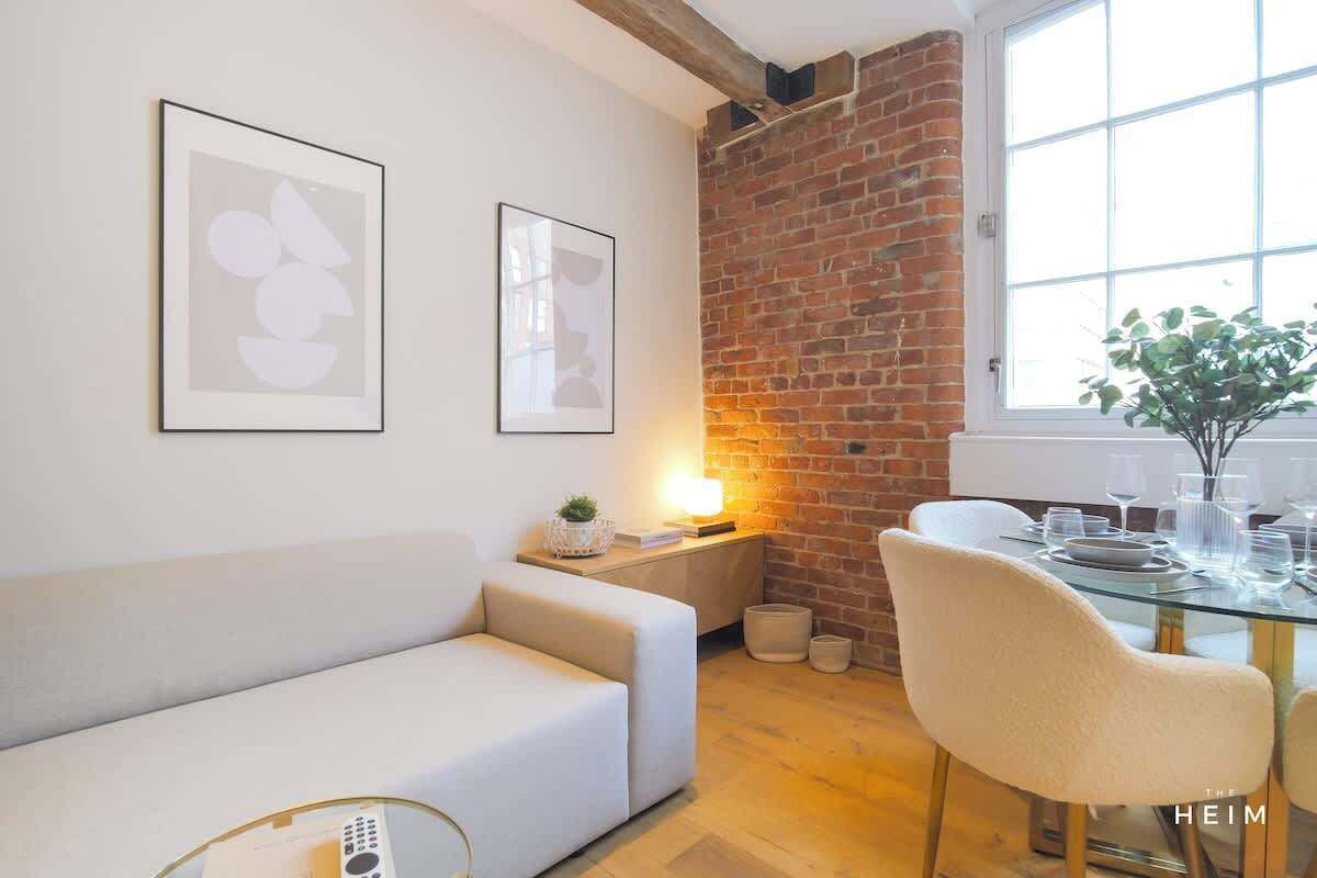 A modern living room with a white sofa, a glass dining table set with plates and glasses, a brick wall, and a large window.