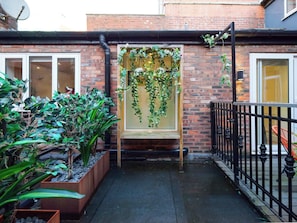 A narrow alleyway with a brick building, a black metal fence, and potted plants. - Dyehouse | The Heim (Greater Manchester)