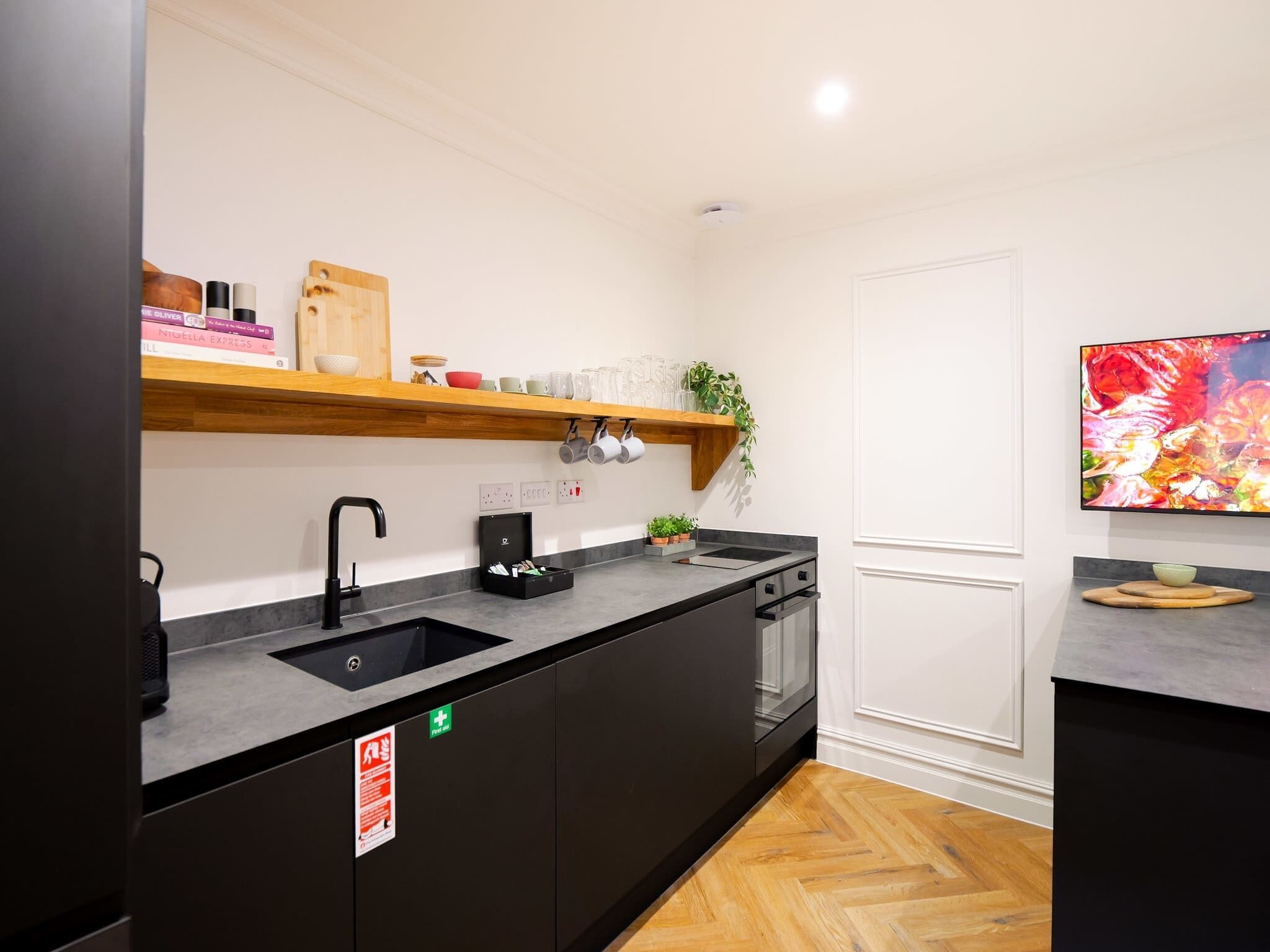 A modern kitchen with a black countertop, wooden shelves, a black sink, and a built-in dishwasher.