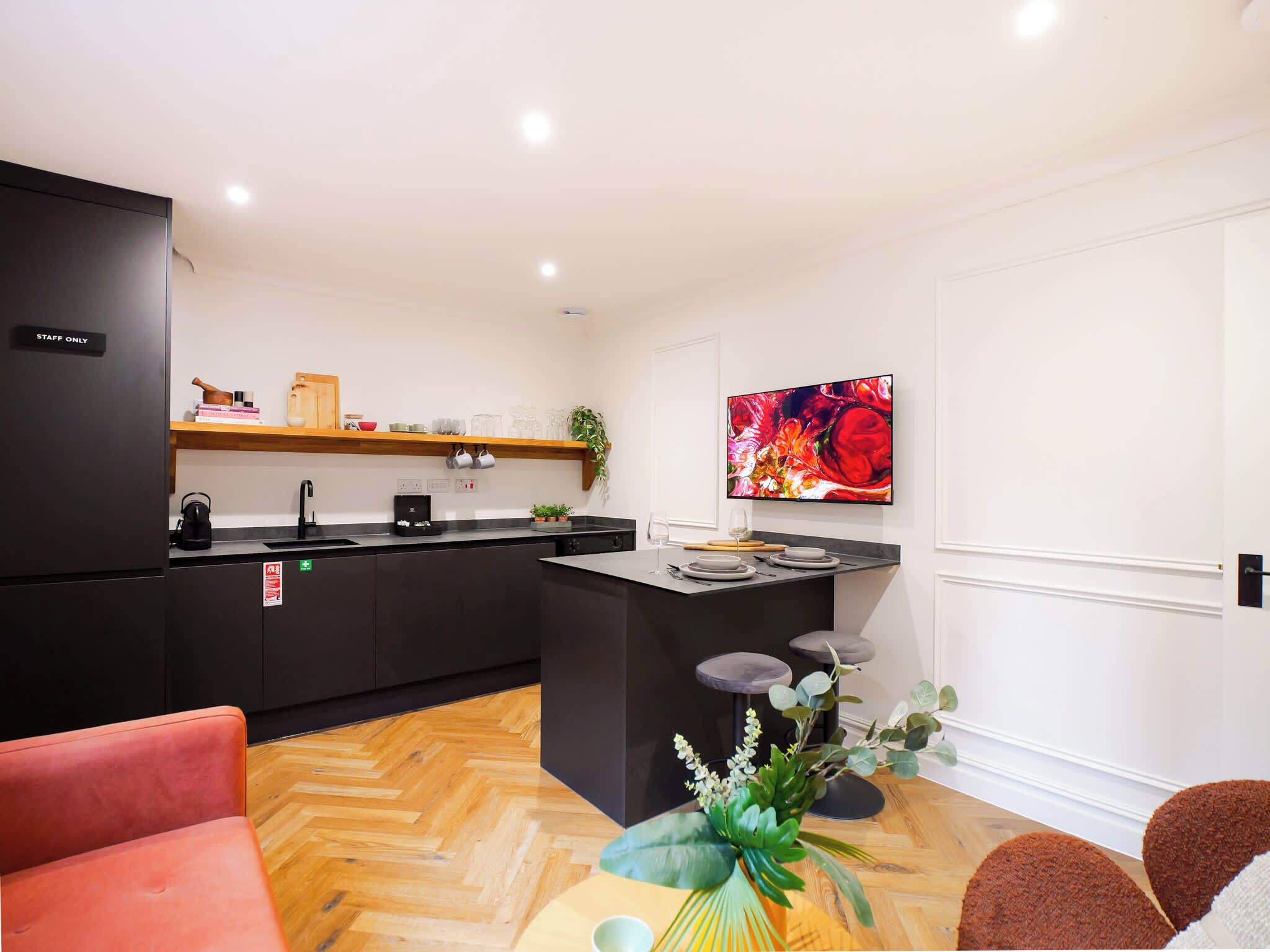 A modern kitchen with a black refrigerator, a wooden shelf, and a dining area with a bar counter.