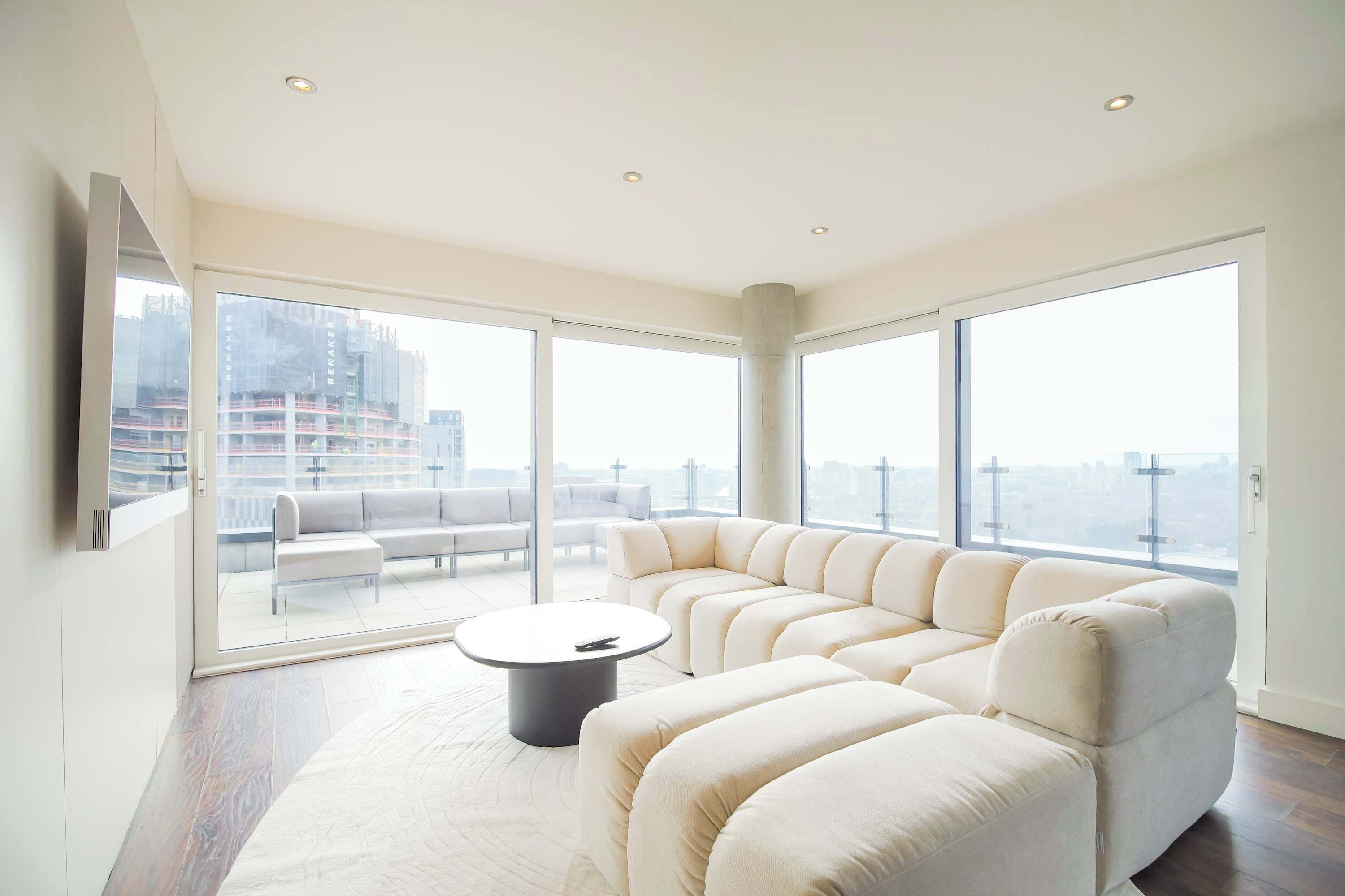 Een moderne woonkamer met een hoekbank, een ronde salontafel en grote ramen van de vloer tot aan het plafond met uitzicht op de stad.