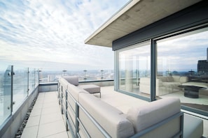 Eine moderne Dachterrasse mit Glasgeländern, einer Sitzecke und Blick auf die Stadt.