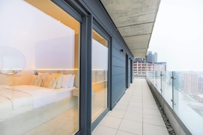 Ein moderner Balkon mit Glasgeländer, einer Couch und einem großen Fenster.