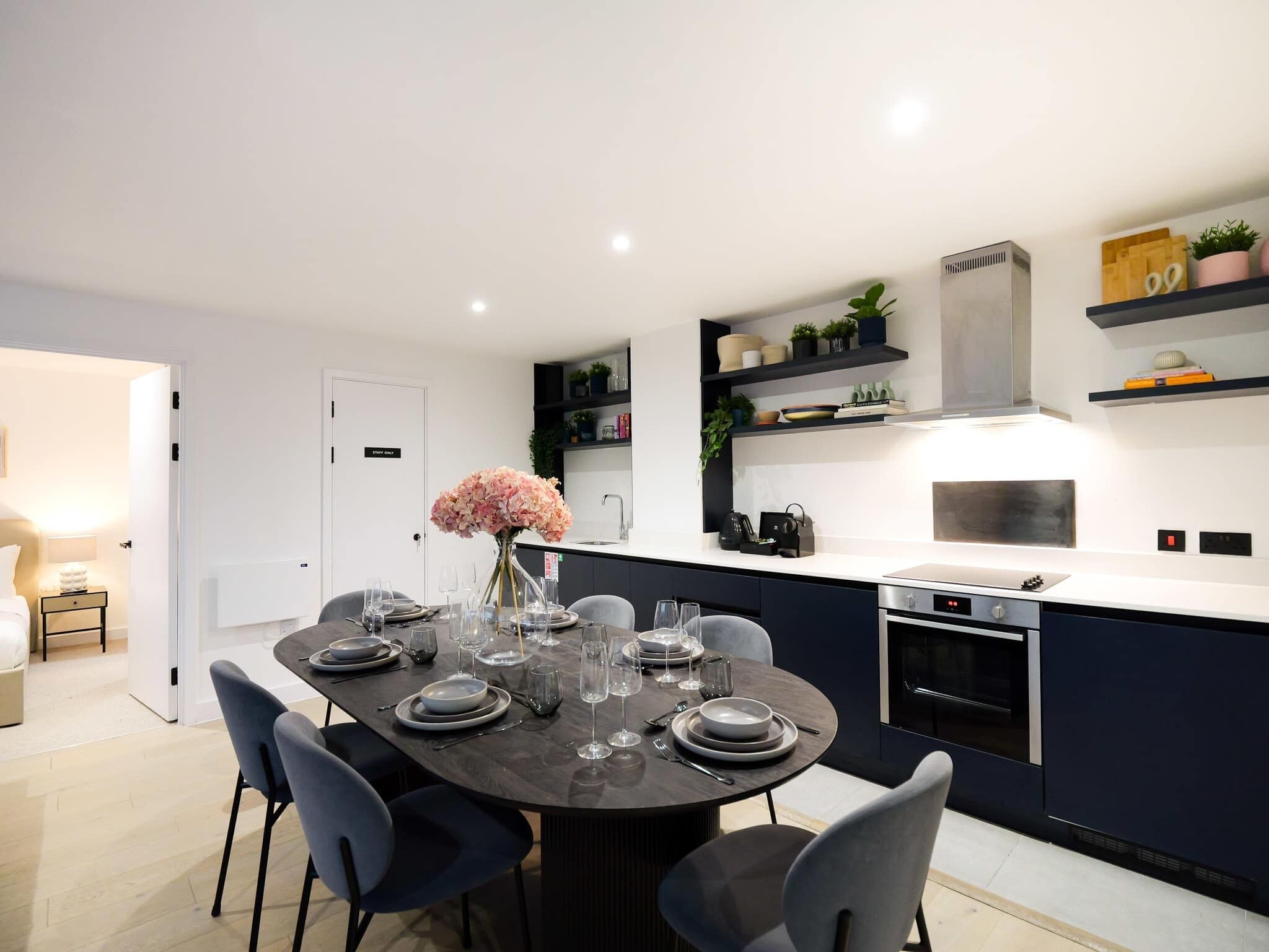 Una cucina moderna con isola centrale, tavolo da pranzo per sei persone e scaffalature integrate con piante.