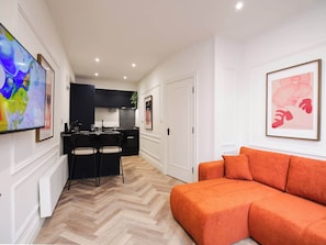 Ein modernes Wohnzimmer mit einer Couch, einem Essbereich mit Stühlen, einer Küche und Kunstwerken an den Wänden.