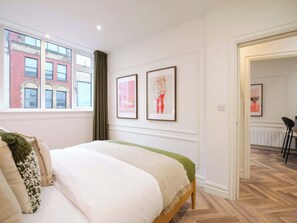 A bedroom with a bed, a window with a view of a brick building, and two framed artworks on the wall. - Calico | The Heim (Greater Manchester)