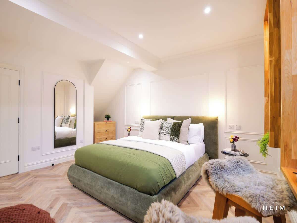 A modern bedroom with a large bed, a wooden bench, a mirror, and a small table with flowers.