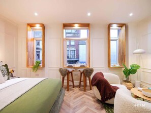 A hotel room with a bed, a desk, two chairs, a window, and a plant. - Merino | The Heim (Greater Manchester)