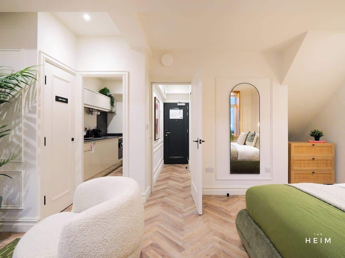 A modern apartment with a kitchen, a bedroom with a green bed, and a mirrored closet.