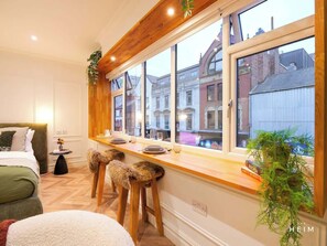Une chambre moderne avec une grande fenêtre, un banc en bois et une table de chevet agrémentée d’une plante.