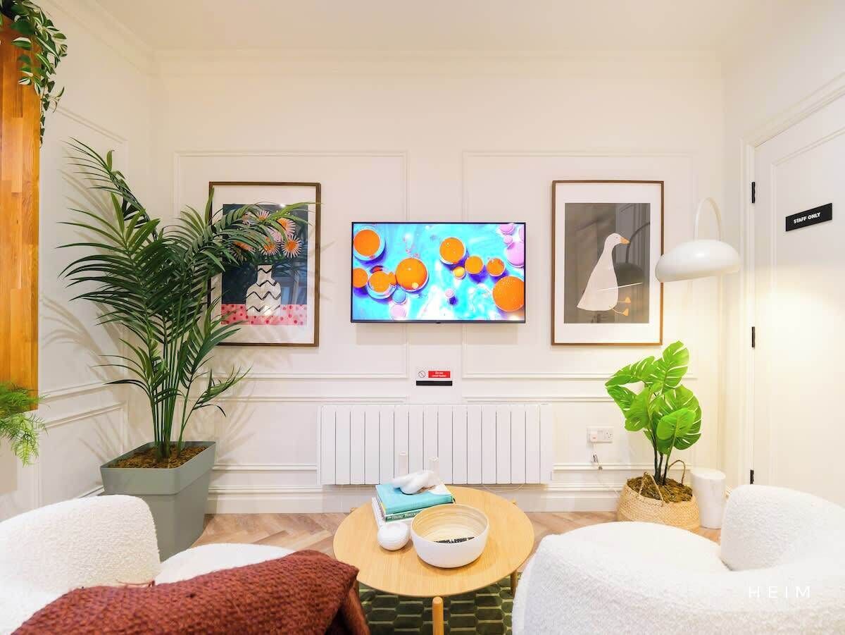 Moderni olohuone, jossa on litteänäyttöinen televisio, kaksi kehystettyä taideteosta, ruukkukasvi ja viihtyisä oleskelualue, jonka keskellä on pyöreä sohvapöytä.