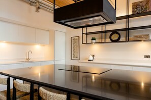 A modern kitchen with a black countertop, white cabinets, and a built-in stove. - Africana | The Heim (Manchester)