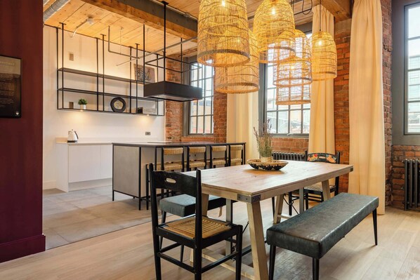 A modern kitchen with a wooden table, black chairs, and wicker pendant lights. - Africana | The Heim (Manchester)