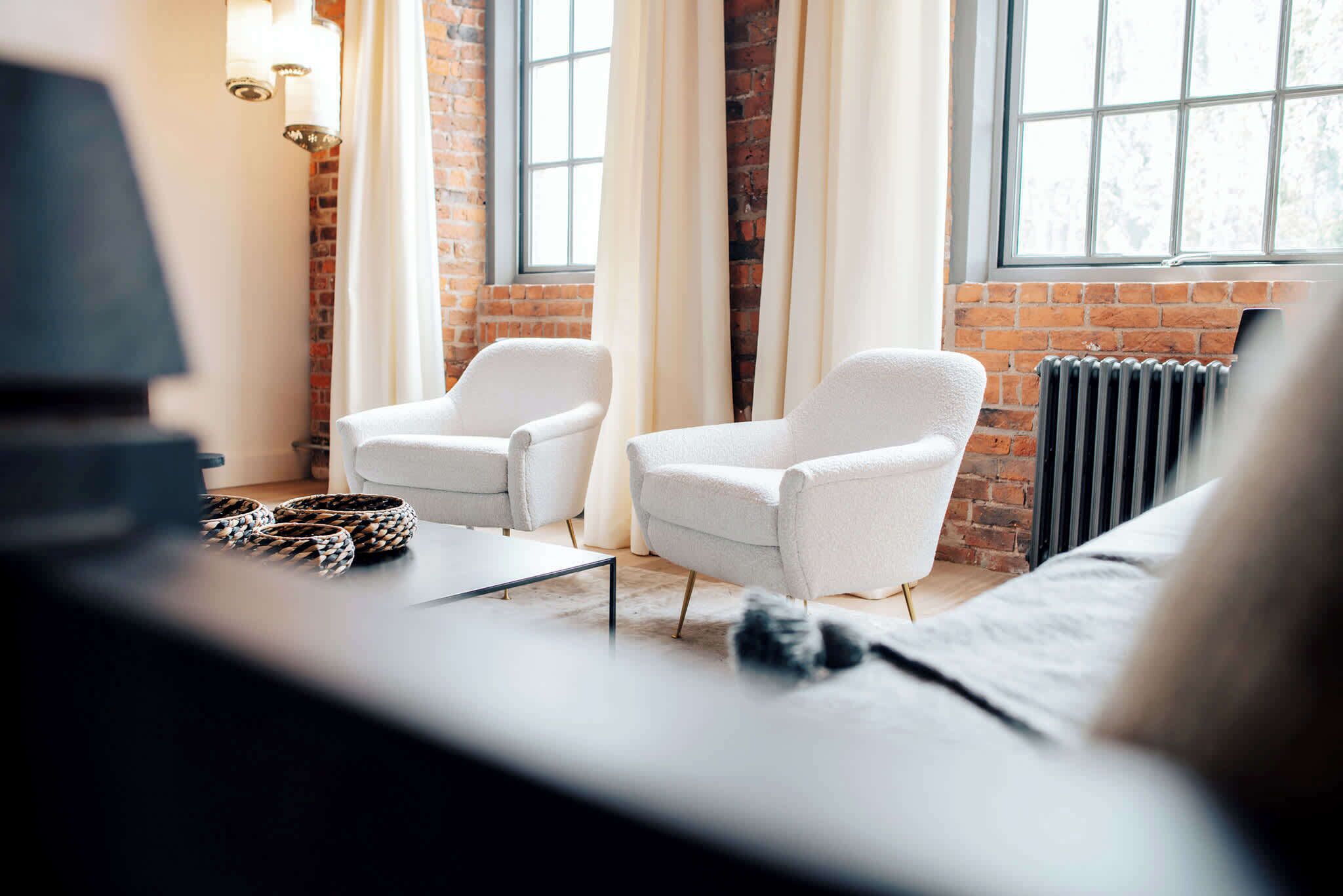 A room with two white armchairs, a sofa, a coffee table, and a lamp.