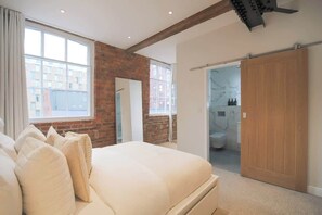 Une chambre avec un grand lit, un mur en briques et une vue sur la ville par une fenêtre.