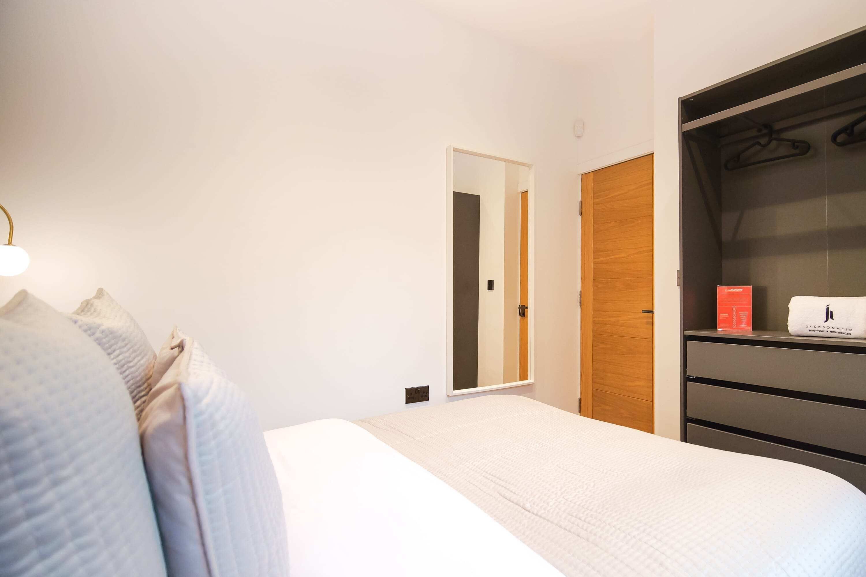 A neatly arranged bedroom with a bed, a wardrobe, and a mirror.