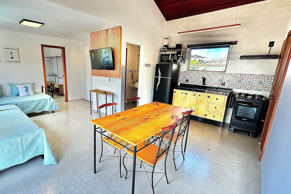 A compact living space with two beds, a dining table, a kitchen area with appliances, and a TV.