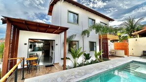 A modern two-story house with a swimming pool, a patio with outdoor furniture, and a garden with tropical plants. - Alto Loft Geribá (Buzios)