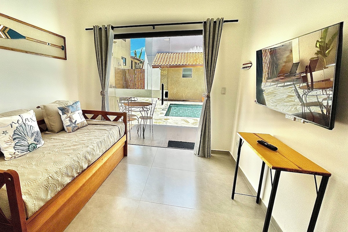A bedroom with a bed, a desk, a chair, and a view of a pool and outdoor area.
